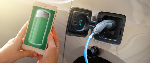 Hands with smartphone on a background of a car at the charging station for electric vehicles....