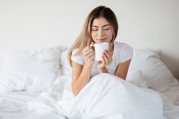 Relaxed woman in bed enjoying the smell of morning coffee