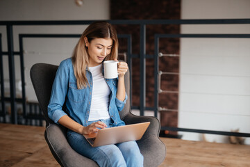 Attractive lady smiling while using her laptop and drinking coffee