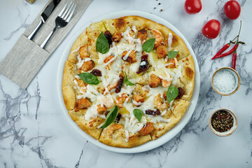 Delicious and crunchy Italian pizza with seafood - salmon and tiger prawns, white sauce and melted cheese in a plate on a marble background. Top view