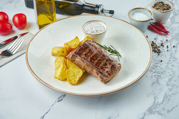 Appetizing beef fillet mignon steak with potato garnish and white sauce, served in a white plate on...