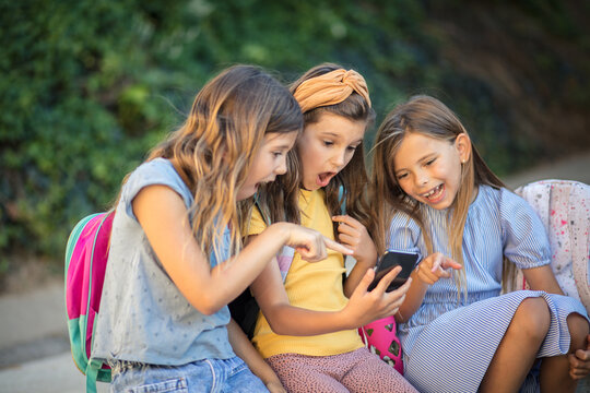  Friends talking and using mobile. Three little girls using smart phone together.