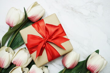 Gift boxes with red ribbon and tulip flower bouquet on marble background