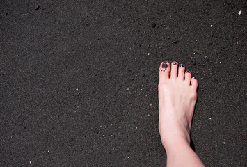 A foot with black color nails on black sand beach