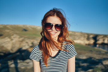 portraits of a red-haired traveler near the river in the mountains blue sky Summer sun adventure