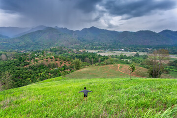 Beautiful landscape with mountains And the village in the middle of the mountain, the top was a black cloud, and it was raining on the mountainside. Farmer boy on the hill has a beautiful green meadow