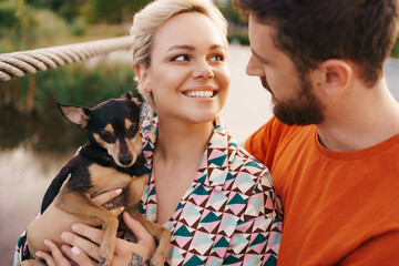 Happy smiling young couple hugging their dog on bridge