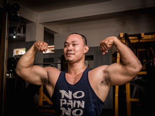 A large and burly man executes a double bicep pose at the gym. Bodybuilding subculture.