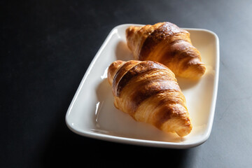 French croissant on white plate on black table background and nature sunlight with shadow through from window.