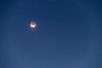 Crescent moon with earthshine is a soft, faint glow on the dark side of the moon and the Pleiades or Seven Sisters in twilight sky.  
