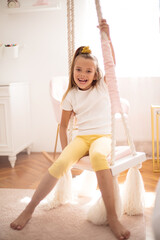 Portrait of smiling little girl on swing in her bedroom.