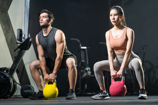 Selective focus at Asian women and men at the background. men swing kettlebell to do crossfit exercise and weight lifting inside fitness gym to workout for physical body strength and firm arms muscle