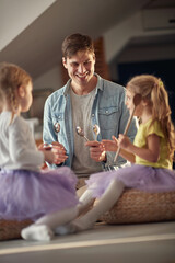 Dad is teaching his little daughters how to drum with spoons on the furniture. Family, home, playing, togetherness