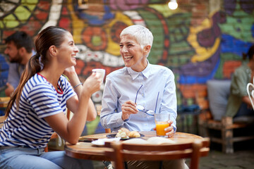 Two happy female friends of different generations having a good time while they have a drink in the...