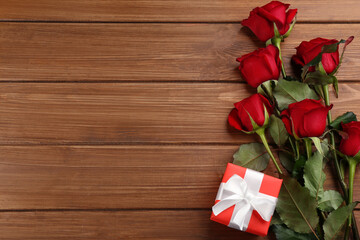 Beautiful red roses and gift box on wooden background, flat lay with space for text. Valentine's Day celebration