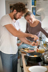young caucasian beardy guy with curly hair making breakfast, while his female partner observing