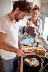 beardy young man with curly hair making breakfast, while his female partner looking with love at him