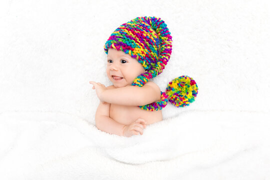 Photo of newborn baby lying on white blanket in big bright funny knitted hat. Adoption concept, happy parenting