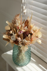 Beautiful dried flower bouquet in glass vase on white windowsill