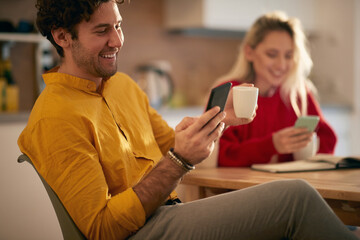 young couple laughing watching their cell phones in the morning, drinking coffee. Modern social distraction concept