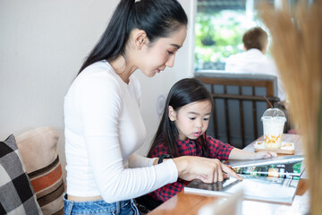 Asian mothers are teaching their daughters to read a book on holidays at home. Educational concepts and activities of the family