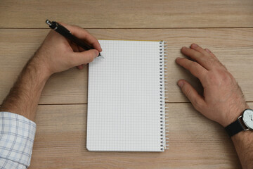 Left-handed man writing in notebook at wooden table, top view