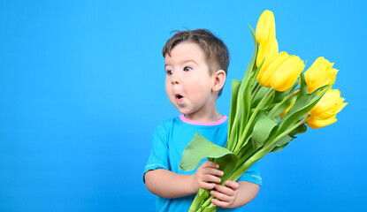 Fun child with bouquet of tulips, surprised boy against a blue wall.