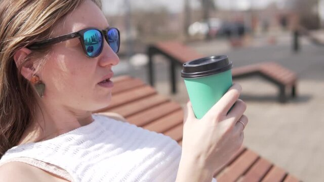 Close-up, a woman drinks coffee from a plastic cup in the spring in the park.