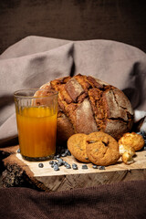 Biscuits, bread and a glass of juice on a wooden stand on a brown background