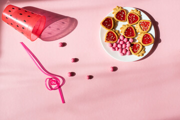 pink candy and cookies, glass and straw for a drink on a pink background