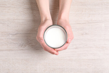 Woman holding glass of milk at white wooden table, top view