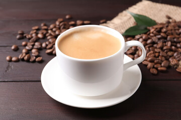 Cup of hot aromatic coffee and roasted beans on wooden table