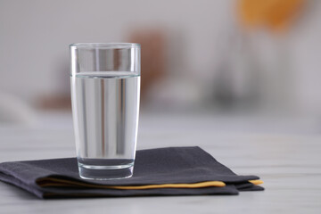 Glass of water and napkins on white table against blurred background. Space for text