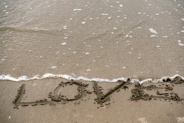 Hand written sign love on a sandy beach washed away by a wave. End of relationship concept. Dark moody colors.