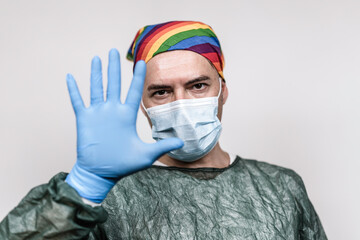 Surgeon doctor with protective mask and rainbow bandanna on his head who is showing his hand in blue glove - Doctor stopping hiv virus or coronavirus with prevention - Lgbtq people rights concept