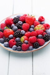 Fresh berry salad on blue dishes. Vintage wooden background.