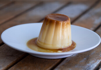 white plate with flan on wooden background, close up view