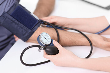 Doctor checking blood pressure of man in clinic, closeup