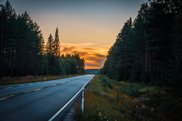 Empty road to the sunset in Finland. Forest on both sides of the road.