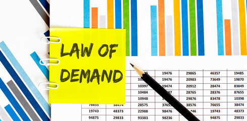 Yellow sticker with text LAW OF DEMAND on chart with pencil .