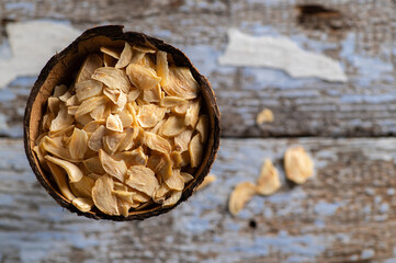 fragrant dry garlic in flakes in a coconut bowl on an old wooden background, top view, empty space...