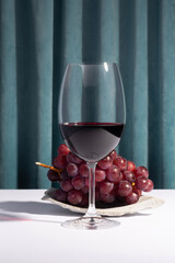Wine glass and grapes on a concrete podium over blue curtain background