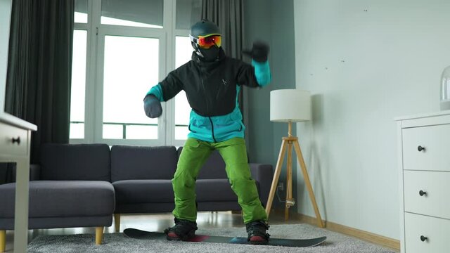 Fun video. Man dressed as a snowboarder depicts snowboarding on a carpet in a cozy room. Waiting for a snowy winter. Slow motion