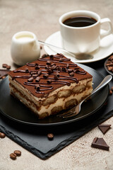 Portion of Traditional Italian Tiramisu dessert and cup of espresso coffee on grey concrete background