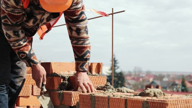 Close up of a man building a brick house. Laying red bricks on a construction site on a sunny day. House construction close up.