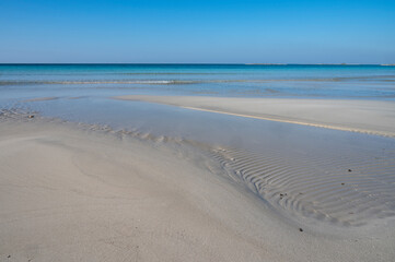 Sabbia bianca con mare trasparente e cielo azzurro.