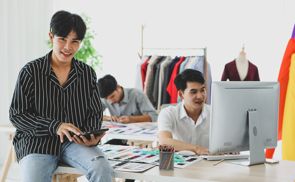 Asian tailor with tablet sitting near coworkers
