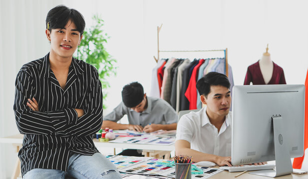 Asian tailor with tablet sitting near coworkers
