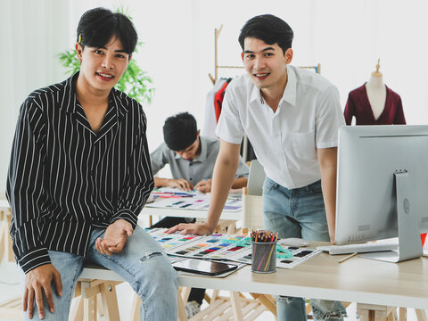 Asian tailor with tablet sitting near coworkers