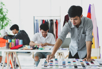 Asian tailor cutting fabric near colleagues